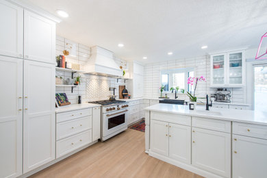 Large transitional l-shaped eat-in kitchen in Other with a farmhouse sink, shaker cabinets, white cabinets, quartz benchtops, white splashback, ceramic splashback, white appliances, vinyl floors, with island, brown floor and white benchtop.