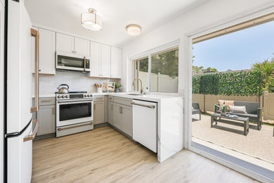 Inspiration for a large contemporary u-shaped laminate floor and brown floor eat-in kitchen remodel in San Diego with an undermount sink, shaker cabinets, white cabinets, quartz countertops, white backsplash, ceramic backsplash, white appliances, no island and white countertops
