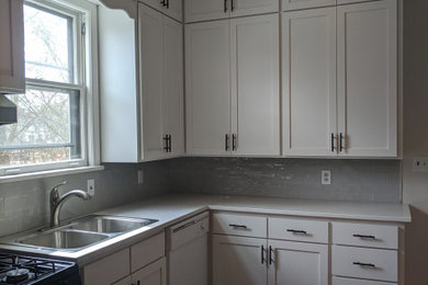 Example of a mid-sized arts and crafts l-shaped laminate floor and brown floor enclosed kitchen design in Minneapolis with a double-bowl sink, shaker cabinets, white cabinets, quartz countertops, gray backsplash, ceramic backsplash and white countertops
