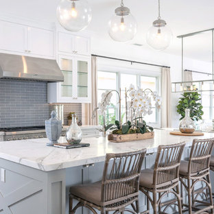 Diseño de cocina marinera con encimera de mármol, salpicadero verde, una isla, armarios con rebordes decorativos, puertas de armario blancas, salpicadero de azulejos tipo metro, electrodomésticos de acero inoxidable y suelo de madera oscura