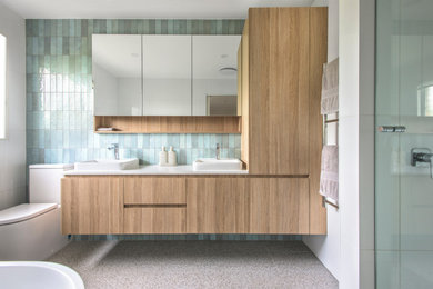 Photo of a mid-sized contemporary master bathroom in Melbourne with glass-front cabinets, light wood cabinets, a freestanding tub, an alcove shower, a two-piece toilet, green tile, subway tile, green walls, porcelain floors, a drop-in sink, engineered quartz benchtops, grey floor, a hinged shower door, white benchtops, a double vanity and a built-in vanity.
