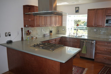 Photo of a mid-sized traditional l-shaped kitchen pantry in Los Angeles with an undermount sink, raised-panel cabinets, medium wood cabinets, quartz benchtops, multi-coloured splashback, glass tile splashback, stainless steel appliances, medium hardwood floors, a peninsula and brown floor.