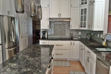 Example of a large transitional l-shaped medium tone wood floor and brown floor kitchen design in Boston with an undermount sink, raised-panel cabinets, white cabinets, granite countertops, gray backsplash, glass tile backsplash, stainless steel appliances and an island