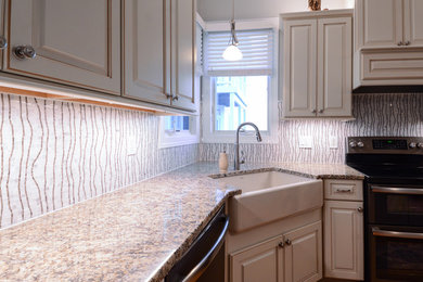 Mid-sized transitional l-shaped medium tone wood floor and brown floor eat-in kitchen photo in Raleigh with a farmhouse sink, raised-panel cabinets, white cabinets, granite countertops, multicolored backsplash, black appliances, an island and mosaic tile backsplash
