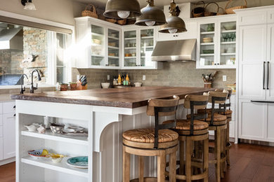 This is an example of an arts and crafts l-shaped eat-in kitchen in San Luis Obispo with a farmhouse sink, shaker cabinets, white cabinets, granite benchtops, beige splashback, stone tile splashback, panelled appliances, dark hardwood floors, with island, brown floor and beige benchtop.
