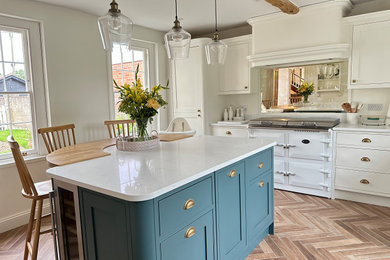 Medium sized farmhouse single-wall enclosed kitchen in Essex with an island, recessed-panel cabinets, white cabinets, marble worktops, white appliances, laminate floors, brown floors, white worktops, exposed beams and feature lighting.