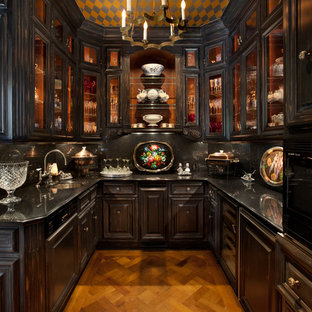 Cette photo montre une petite arrière-cuisine méditerranéenne en U avec un évier encastré, un placard à porte vitrée, des portes de placard noires, une crédence noire, un sol en bois brun, un plan de travail en granite, aucun îlot et un électroménager encastrable.