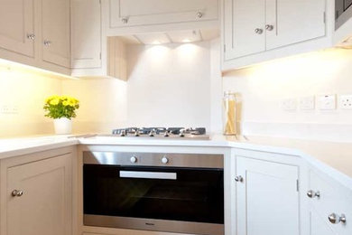 Photo of a small traditional u-shaped separate kitchen in London with a farmhouse sink, shaker cabinets, white cabinets, stainless steel appliances and medium hardwood floors.