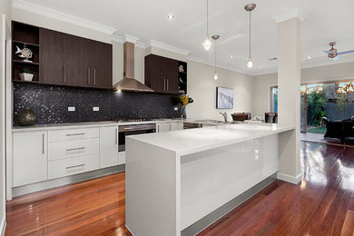 Photo of a mid-sized contemporary u-shaped open plan kitchen in Melbourne with a double-bowl sink, flat-panel cabinets, white cabinets, granite benchtops, black splashback, mosaic tile splashback, stainless steel appliances, medium hardwood floors and a peninsula.