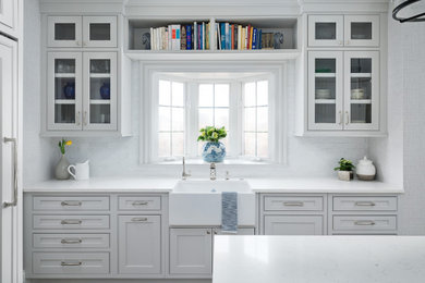 Example of a large transitional u-shaped medium tone wood floor and brown floor enclosed kitchen design in Chicago with a farmhouse sink, beaded inset cabinets, gray cabinets, quartz countertops, white backsplash, porcelain backsplash, paneled appliances, an island and white countertops