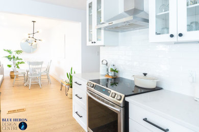 Example of a mid-sized danish l-shaped beige floor eat-in kitchen design in Other with an undermount sink, shaker cabinets, white cabinets, quartz countertops, white backsplash, subway tile backsplash, stainless steel appliances, an island and white countertops