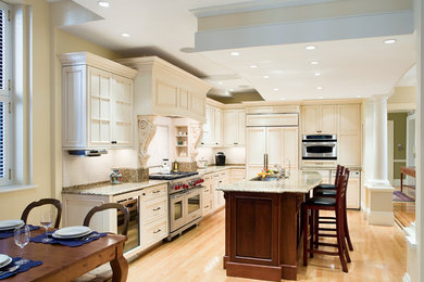 Mid-sized elegant l-shaped light wood floor eat-in kitchen photo in Boston with an undermount sink, recessed-panel cabinets, white cabinets, granite countertops, beige backsplash, travertine backsplash, stainless steel appliances, an island and beige countertops