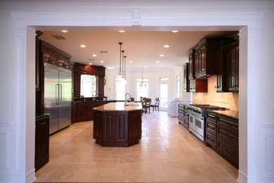 Example of a classic eat-in kitchen design in New York with an undermount sink, raised-panel cabinets, dark wood cabinets, granite countertops, beige backsplash, subway tile backsplash and stainless steel appliances