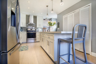 Mid-sized trendy l-shaped porcelain tile eat-in kitchen photo in Miami with an undermount sink, shaker cabinets, white cabinets, quartz countertops, gray backsplash, glass tile backsplash, stainless steel appliances and an island