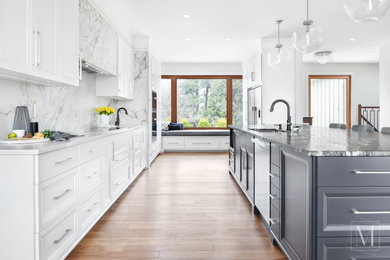This is an example of a large contemporary galley kitchen/diner in Toronto with a submerged sink, white cabinets, engineered stone countertops, white splashback, marble splashback, stainless steel appliances, light hardwood flooring, a breakfast bar, brown floors and black worktops.