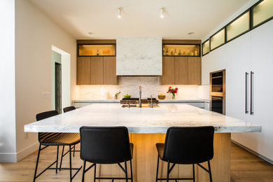 Design ideas for a mid-sized modern kitchen in Denver with an undermount sink, flat-panel cabinets, marble benchtops, white splashback, marble splashback, white appliances, light hardwood floors, with island and white benchtop.