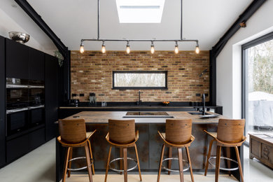 Photo of a medium sized urban l-shaped open plan kitchen in Sussex with flat-panel cabinets, black cabinets, engineered stone countertops, black appliances, concrete flooring, an island, black worktops and feature lighting.