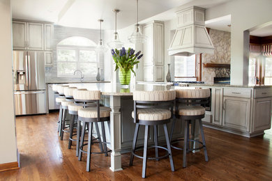 Inspiration for a large transitional l-shaped medium tone wood floor and brown floor open concept kitchen remodel in Milwaukee with an undermount sink, white cabinets, granite countertops, gray backsplash, stainless steel appliances and an island