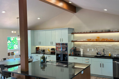 Example of a mid-sized trendy l-shaped laminate floor, brown floor and vaulted ceiling eat-in kitchen design in Seattle with flat-panel cabinets, medium tone wood cabinets, quartzite countertops, multicolored backsplash, subway tile backsplash, stainless steel appliances, an island and black countertops