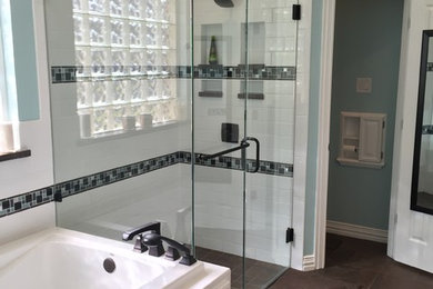 Inspiration for a mid-sized transitional master bathroom in Dallas with raised-panel cabinets, white cabinets, a drop-in tub, a curbless shower, brown tile, stone slab, solid surface benchtops, a hinged shower door, a two-piece toilet, blue walls, ceramic floors, an undermount sink and brown floor.