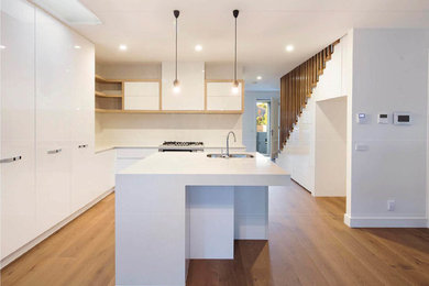 Design ideas for a mid-sized modern l-shaped separate kitchen in Melbourne with white splashback, with island, white benchtop, white cabinets and solid surface benchtops.