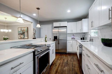 Mid-sized trendy l-shaped dark wood floor eat-in kitchen photo in Other with a double-bowl sink, shaker cabinets, white cabinets, white backsplash, stainless steel appliances and an island