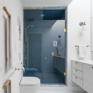 Idee per una piccola stanza da bagno padronale minimalista con doccia alcova, WC sospeso, pareti bianche, pavimento in marmo, lavabo sottopiano, top in marmo, ante lisce, ante bianche, porta doccia a battente, piastrelle blu, piastrelle di vetro e pavimento grigio