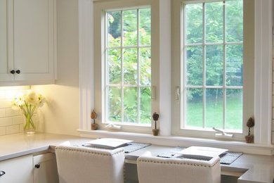 U-shaped light wood floor eat-in kitchen photo in New York with a farmhouse sink, recessed-panel cabinets, white cabinets, quartz countertops, white backsplash, subway tile backsplash, stainless steel appliances and gray countertops