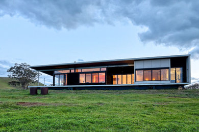 Photo of a modern one-storey black house exterior in Melbourne with wood siding, a flat roof and a metal roof.