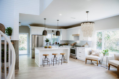 Mid-sized beach style l-shaped open plan kitchen in San Diego with an undermount sink, shaker cabinets, white cabinets, quartz benchtops, white splashback, ceramic splashback, stainless steel appliances, ceramic floors, with island and brown floor.