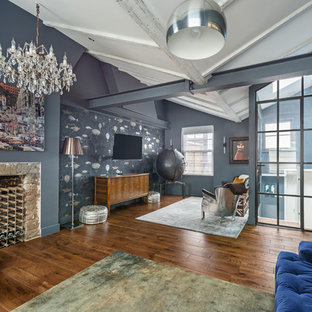Industrial open plan family and games room in London with blue walls, light hardwood flooring, a standard fireplace, a stone fireplace surround, a wall mounted tv and brown floors.