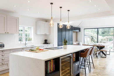Large modern open plan kitchen in Other with a submerged sink, shaker cabinets, blue cabinets, quartz worktops, stainless steel appliances, laminate floors, an island, white worktops and a feature wall.