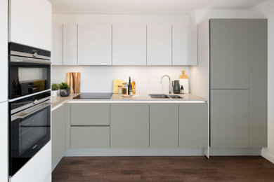 Design ideas for a medium sized contemporary l-shaped open plan kitchen in London with an integrated sink, flat-panel cabinets, green cabinets, composite countertops, white splashback, limestone splashback, integrated appliances, dark hardwood flooring, no island, brown floors and beige worktops.