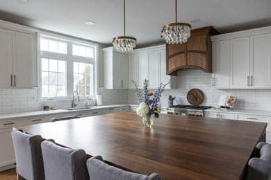 Large elegant medium tone wood floor open concept kitchen photo in Philadelphia with an undermount sink, recessed-panel cabinets, wood countertops, white backsplash, porcelain backsplash, stainless steel appliances and an island