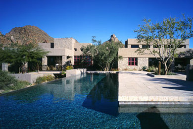 Diseño de piscina infinita moderna extra grande en forma de L en patio trasero con adoquines de hormigón