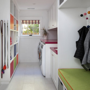サンフランシスコのミッドセンチュリースタイルのおしゃれな家事室 (シェーカースタイル扉のキャビネット、白いキャビネット、人工大理石カウンター、白い壁、セラミックタイルの床、左右配置の洗濯機・乾燥機、白い床、赤いキッチンカウンター) の写真