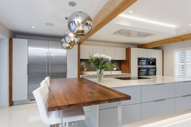 This is an example of a contemporary kitchen in Sussex with flat-panel cabinets, grey cabinets, grey splashback, ceramic flooring, an island and white floors.