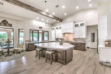 Photo of a large country l-shaped eat-in kitchen in Phoenix with a farmhouse sink, raised-panel cabinets, brown cabinets, quartz benchtops, white splashback, porcelain splashback, stainless steel appliances, porcelain floors, with island, brown floor and white benchtop.