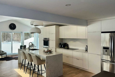 Example of a large minimalist single-wall light wood floor and brown floor open concept kitchen design in Montreal with an undermount sink, flat-panel cabinets, white cabinets, quartz countertops, white backsplash, quartz backsplash, stainless steel appliances, an island and white countertops