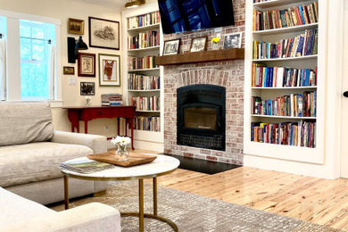 Cette image montre une salle de séjour rustique de taille moyenne et ouverte avec une bibliothèque ou un coin lecture, un mur blanc, parquet clair, un poêle à bois, un manteau de cheminée en brique, un téléviseur fixé au mur, un sol marron et un plafond en lambris de bois.