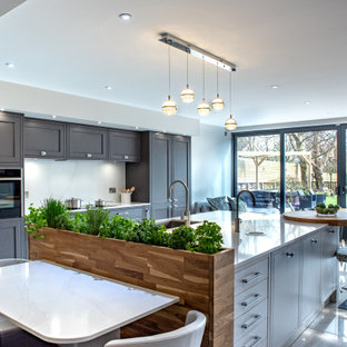 Photo of a large contemporary galley kitchen in Other with a submerged sink, shaker cabinets, grey cabinets, white splashback, stainless steel appliances, an island, white floors and white worktops.