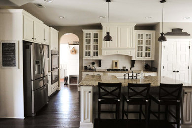 Mid-sized elegant l-shaped dark wood floor enclosed kitchen photo in Atlanta with a farmhouse sink, white backsplash, subway tile backsplash, stainless steel appliances, glass-front cabinets, white cabinets, granite countertops and an island