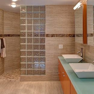 Réalisation d'une salle de bain principale minimaliste de taille moyenne avec un placard à porte plane, des portes de placard en bois brun, une baignoire posée, un carrelage beige, un mur beige, un sol en calcaire, une vasque, un plan de toilette en verre et du carrelage en pierre calcaire.