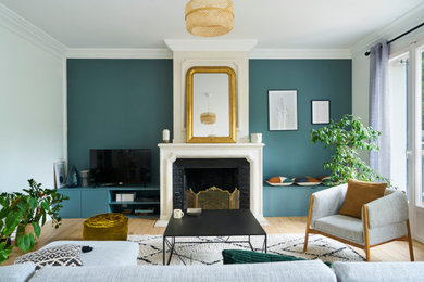 Exemple d'un salon chic de taille moyenne et ouvert avec un mur bleu, parquet clair, une cheminée standard, un manteau de cheminée en pierre, un téléviseur indépendant et un sol beige.