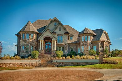 Large mountain style three-story stone exterior home photo in Raleigh with a hip roof
