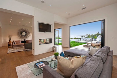Example of a large minimalist open concept medium tone wood floor living room design in Los Angeles with white walls, a two-sided fireplace, a plaster fireplace and a wall-mounted tv