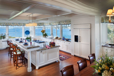Inspiration for a large beach style l-shaped open plan kitchen in Boston with an undermount sink, shaker cabinets, white cabinets, granite benchtops, stainless steel appliances, medium hardwood floors, with island, brown floor and window splashback.