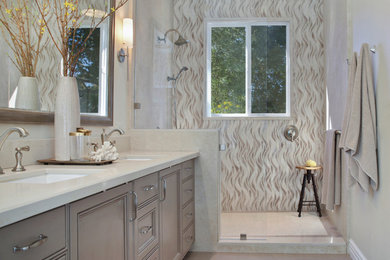 Inspiration for a mid-sized transitional master stone tile ceramic tile and beige floor bathroom remodel in Orange County with recessed-panel cabinets, gray cabinets, quartz countertops, beige walls, a drop-in sink and a hinged shower door