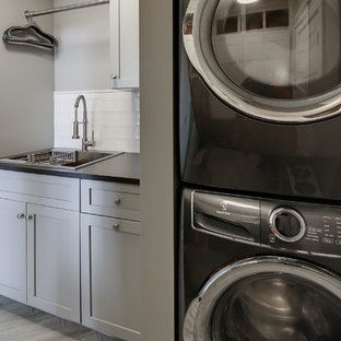 ダラスの小さいトランジショナルスタイルのおしゃれな洗濯室 (ドロップインシンク、シェーカースタイル扉のキャビネット、グレーのキャビネット、クオーツストーンカウンター、グレーの壁、ラミネートの床、上下配置の洗濯機・乾燥機、グレーの床、黒いキッチンカウンター) の写真