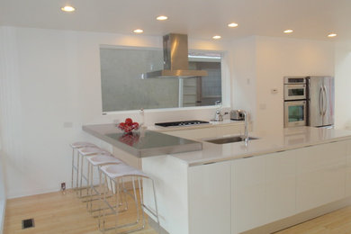 Example of a mid-sized trendy l-shaped light wood floor enclosed kitchen design in Chicago with an undermount sink, shaker cabinets, white cabinets, stainless steel countertops, white backsplash, stainless steel appliances and an island